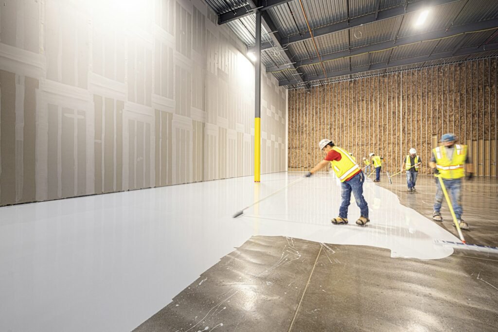 Workers rolling a coating onto a large concrete floor